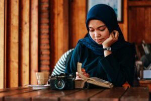 muslim woman in hijab reading quran with a camera on the table in front of her