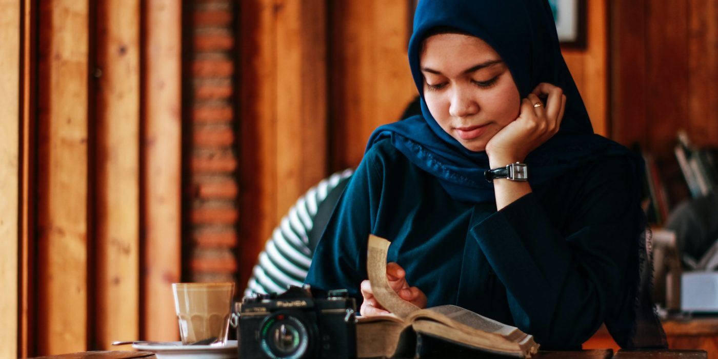 muslim woman in hijab reading quran with a camera on the table in front of her